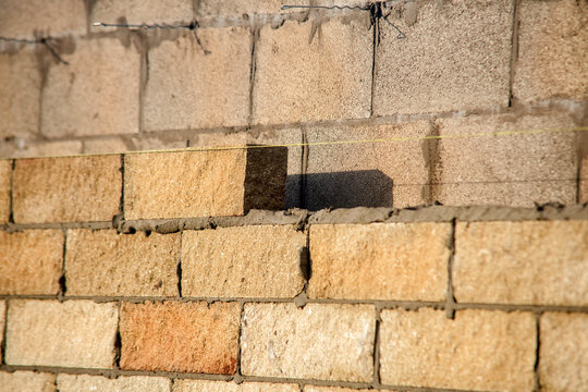 Construction workers build a brick wall at a construction site in the afternoon sunlight with materials and tools nearby