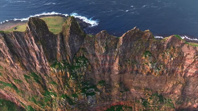 Overhead drone lateral slide to right above towering volcanic basalt cliffs near Torshavn in the Faroe Islands, with visible erosion layers, Atlantic wave exposure and North Atlantic coastal geology.