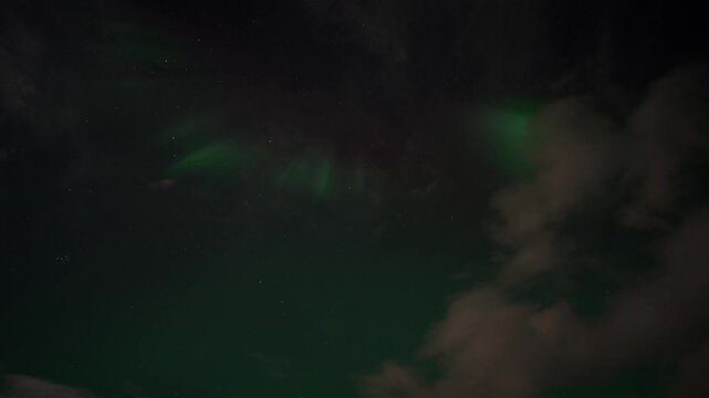 Green aurora borealis moving across the Arctic night sky above Iceland with visible stars, geomagnetic plasma bands and drifting cloud formations, upward pitch timelapse shot.