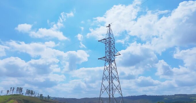 Steel lattice electrical transmission tower above rolling pasture hills near Santo Ant&ocirc;nio do Monte, Minas Gerais, Brazil with orbit parallax movement revealing rural terrain and utility corridor