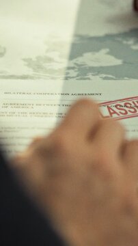 In a formal ministry office, a male civil servant examines a confidential government document with an official seal, underscoring bureaucratic authority and careful handling of sensitive records