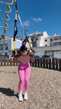 Caucasian female engaged in upper body TRX workout outdoors under clear sky