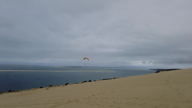Cinematic shot of a paraglider soaring in the sky over the Dune of Pyla, travel footage