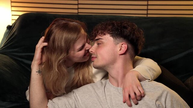 This depicts the intimate connection and affectionate moments of a young couple on a sofa, embodying a romantic relationship and love concept. The man and woman are seen in a close embrace, sharing ge