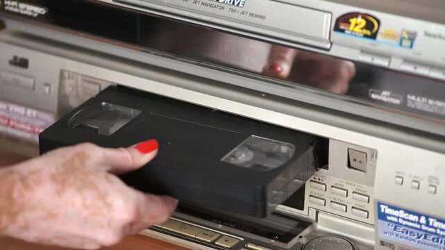 Ukraine, Vinnytsia. June 25 2025.Transportation College. Close-up of a woman&rsquo;s hand with red manicure inserting a VHS cassette into a vintage VCR player. Retro home entertainment technology concept, n