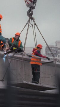 Construction workers in hard hats and safety vests work side-by-side high above a concrete road bridge, repairing its surface. Their effort emphasizes safety, precision, and expert bridge maintenance