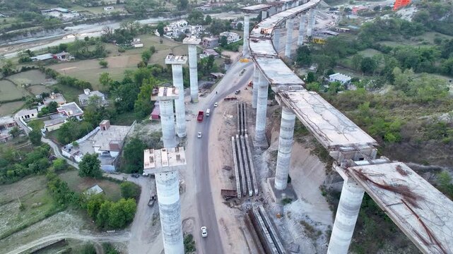High angle view of curved unfinished highway bridge construction showing giant concrete pillars for new flyover. The immense scale of the new highway supports completely dwarfs the existing old road