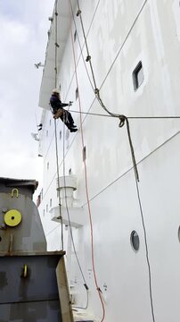 team of ship deck crew working aloft for painting forward part of superstructure. seafarers hang on ropes and bosun chair. team work and cooperation.