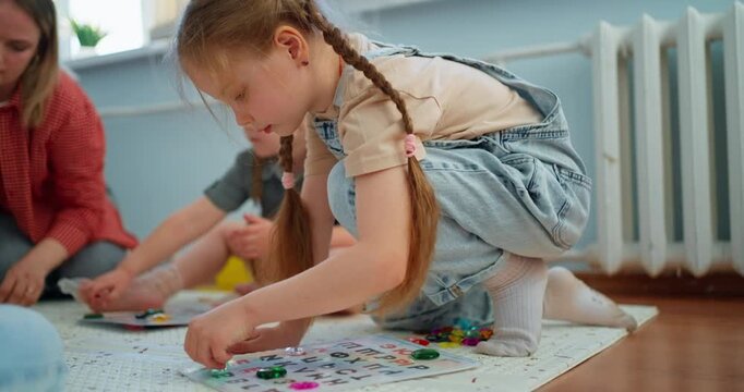 Young children and teacher sitting on classroom floor playing colorful educational board games together during an engaging early learning activity