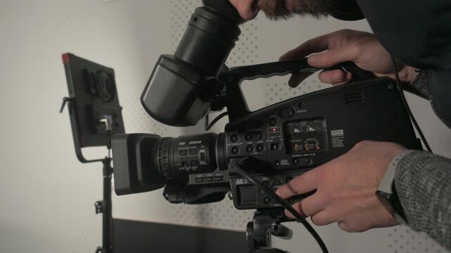 Close-up of a videographer adjusting audio levels and settings on a professional video camera in a studio environment.