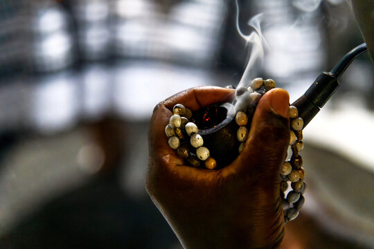A woman's hand holding a rosary and a pipe with smoke coming out of it.