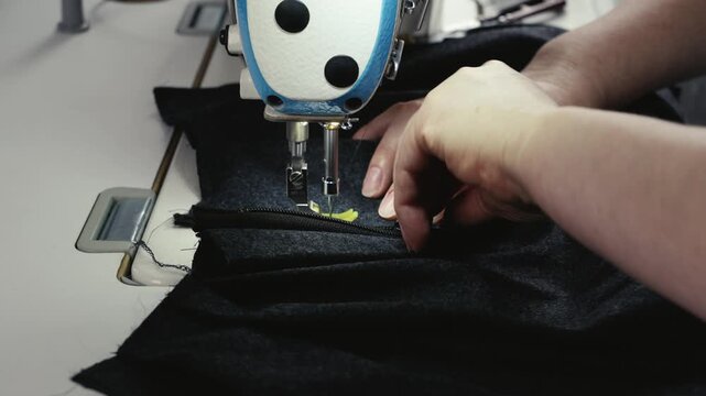 Close up of hands sewing fabric on sewing machine at home workshop. Tailoring process, textile work and handmade clothing production concept.