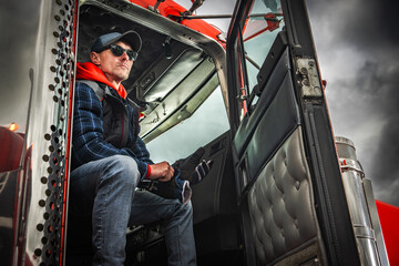 Naklejka premium Driver sits in truck cab, preparing for journey on a cloudy day