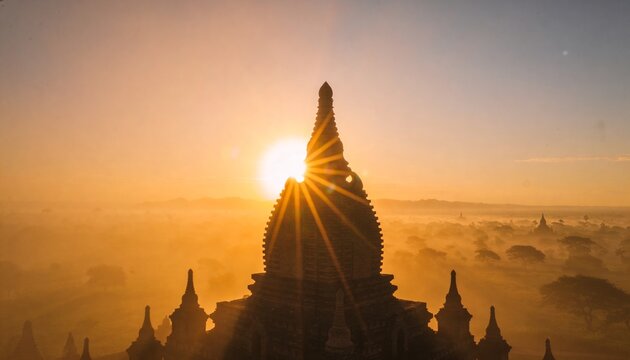 Framing large ornate temple spire silhouette at dawn glowing behind rising sun, mist veiling plain
