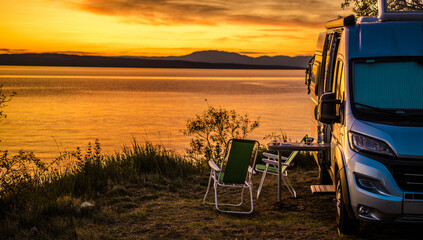 Sunset at campsite by the water with a camper van and chairs nearby © Tomasz Zajda