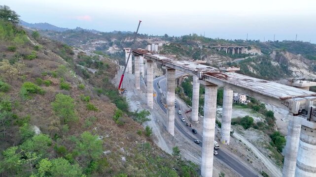 Active civil engineering: Crane lifting materials onto bridge pillars. Dynamic aerial drone footage capturing active heavy civil engineering as a construction crew and a large mobile crane working