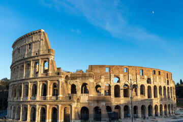 Obraz premium Famous Coliseum in Rome. Colosseum, or Coliseum. Sunset at huge Roman amphitheatre, Rome, Italy, Europe. Famous touristic place in the world and Europe. Beautiful blue sky background.