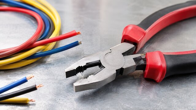 Electrical pliers with colorful wires on metal background representing electrical engineering, cable installation, wiring maintenance, industrial repair, power systems, and electrician tools concept.