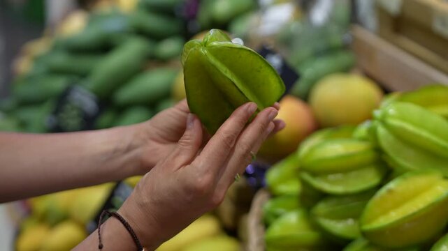 Customer choosing, inspect carambola for buying. Fresh fruit selection, market shopping, travel food choosing, local tropical grocery, juicy fruit choice, checking quality of food. Natural vitamins. 