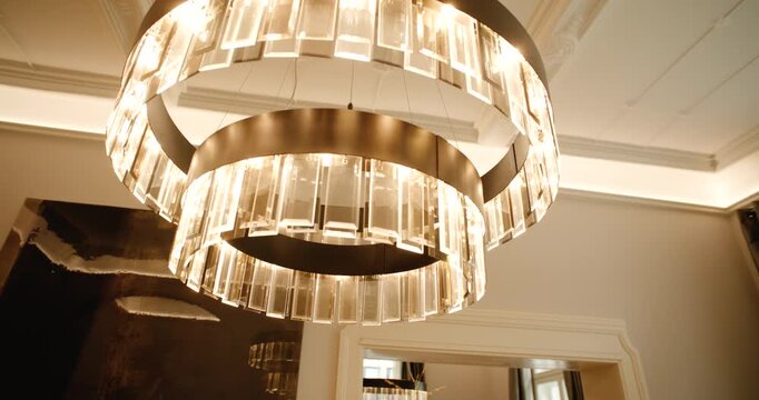 Close up tracking shot of modern luxury crystal chandelier hanging from ceiling inside building