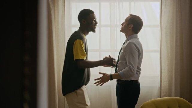 Medium shot of African American and Caucasian doing bro hug while standing in living room and communicating