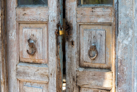 Wooden doors stand ajar with a padlock and knocker in a historic building during daytime