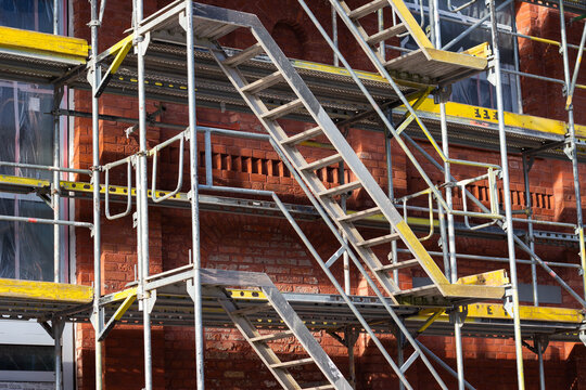 Metal scaffolding structure with multiple staircases against a red brick wall, showcasing construction elements and safety features in an urban environment