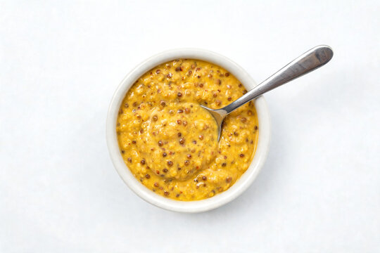 Appetizing whole grain mustard in a white bowl with silver spoon, top down view. Bright clean background. Ideal for culinary, cooking, deli menus, food styling, condiment and recipe design projects.