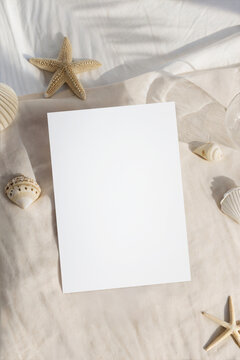 Summer vertical card mockup on beige fabric with palm leaf shadow. Blank beach theme greeting card or invitation template with natural seashells and starfish decor.