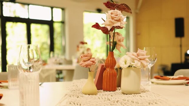 Wedding table centerpiece with elegant floral design in ceramic vases on a boho macrame runner. Slow motion decoration details of a beautiful marriage reception dinner tablescape.