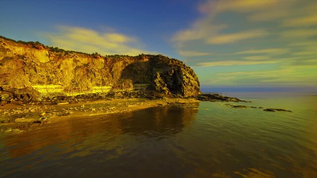 low tide revealing coastal textures and reflective pools, exposed rock shelves and seaweed patches, gentle ripples across shallow water, tranquil study