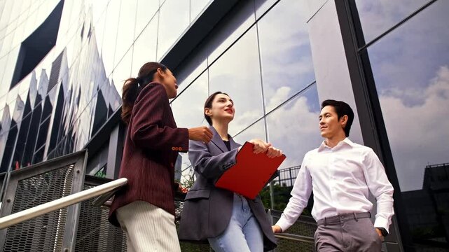 Three professionals converse on outdoor steps beside a modern glass office building, holding documents and smiling, suggesting teamwork and planning in an urban corporate setting.