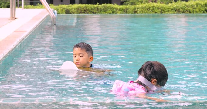 Adorable asian school kids boy and girl enjoy swim practice in resort village swimming pool