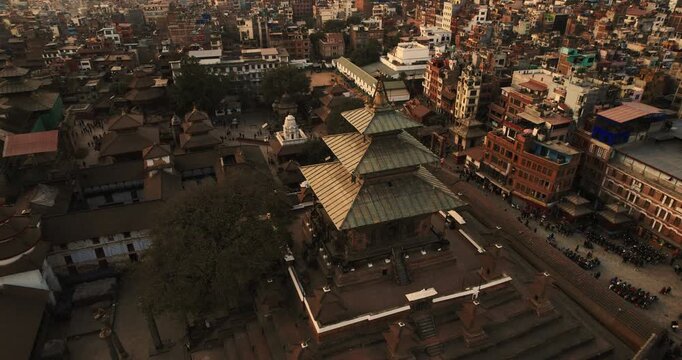Aerial drone shot of an ornate golden-roofed pagoda temple in Basantapur Durbar Square, surrounded by densely packed traditional buildings and crowds gathering at dusk.