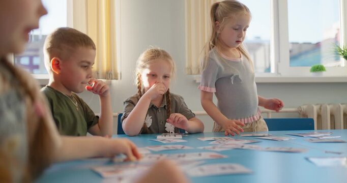 Young children collaborating around a classroom table with illustrated cards during a bright educational group activity by sunny windows