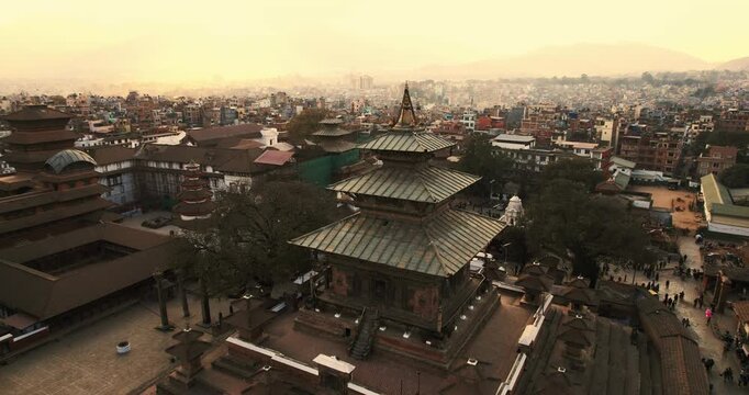 Aerial view of the tiered pagoda roofs of a Newari temple in Bhaktapur Durbar Square, with the historic city sprawling under a hazy golden sky.