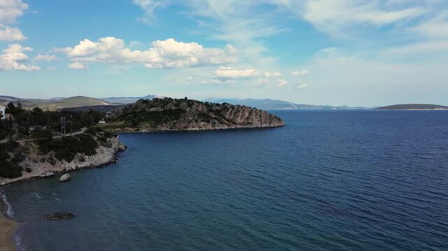 Beautiful 4K drone panoramic view of Tolo sandy beach in Argolis, Greece. Featuring crystal clear blue sea waters, rocky coastal cliffs, small islands and summer resort vibes.