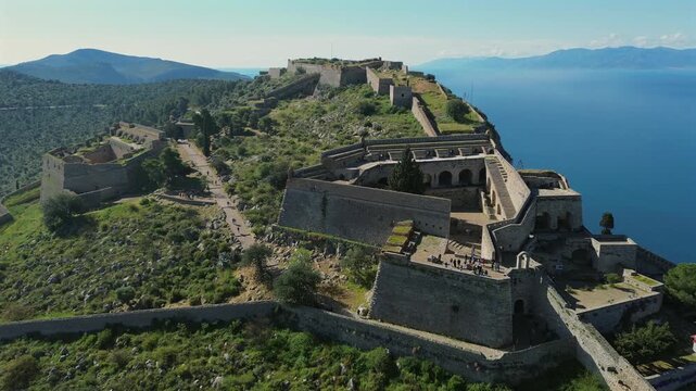 Cinematic 4K drone slow pull-out shot revealing the massive stone battlements of Palamidi Fortress in Nafplio, Greece. Imposing historical architecture over a calm blue sea.
