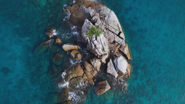 Cinematic top-down drone shot of waves washing over granite boulders and green trees in the vibrant turquoise waters of Anse Soleil, Mahe, Seychelles 30fps 003