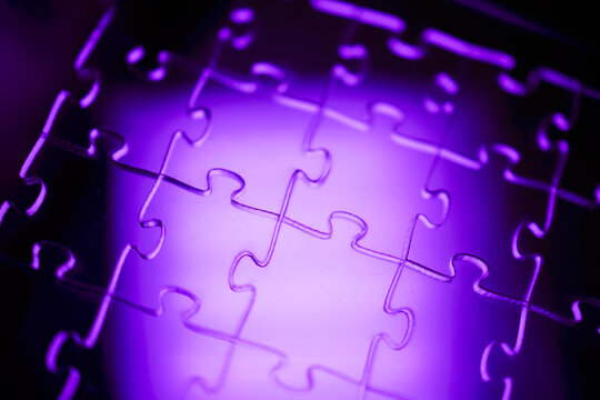Close-up view of interlocking puzzle pieces illuminated with purple light, showcasing the unique shapes and contours of each piece against a soft background