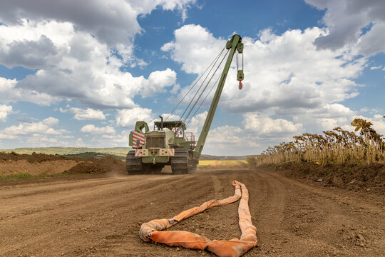 Heavy Crawler Crane Moving on Rural Dirt Road at Pipeline Construction Site