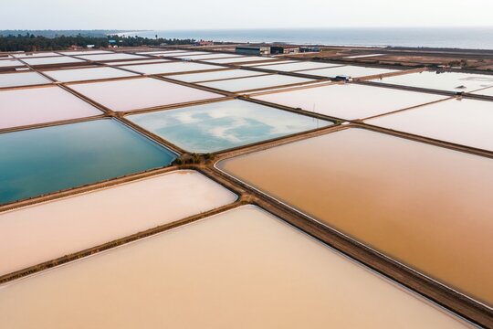 Aerial view salt evaporation ponds in Sri Lanka. Water pools form colorful patterns for salt production. Coastal landscape with sea in background. Natural sea salt harvesting industry.