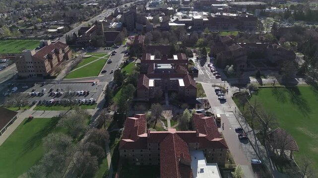 Campus lawn corridor near Colorado Ave, adjacent greens form hyperlocal frame with academic buildings, walkways, parking areas extending residential streets. Redtile roofs, masonry, Boulder, CO