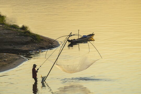 Fisherman with a sinking net at sunset on the Mekong, Luang Prabang, Laos