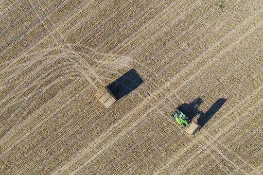 Tractor collecting bales of straw and abstract patterns in cornfield after wheat harvest, aerial view, drone shot, C&oacute;rdoba province, Andalusia, Spain