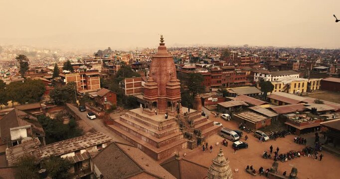 Aerial view of a tall tiered brick shikhara temple rising above the rooftops of Bhaktapur, Nepal, under a soft hazy morning sky.