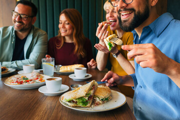 Friends eating sandwiches and drinking coffee at restaurant table