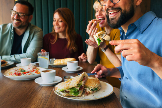 Friends eating sandwiches and drinking coffee at restaurant table