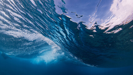 Underwater view inside a breaking ocean wave, forming a blue barrel with white foam and dynamic water textures © Dudarev Mikhail