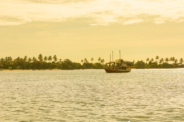 Obraz premium High quality tropical sunset landscape at Rio de Contas in Itacare Bahia Brazil featuring a boat crossing calm reflective waters with intense golden sunlight dramatic sky and realistic ocean reflectio